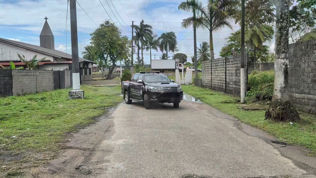 A police vehicle parked on a residential road, lined with palm trees and a church in the background.
