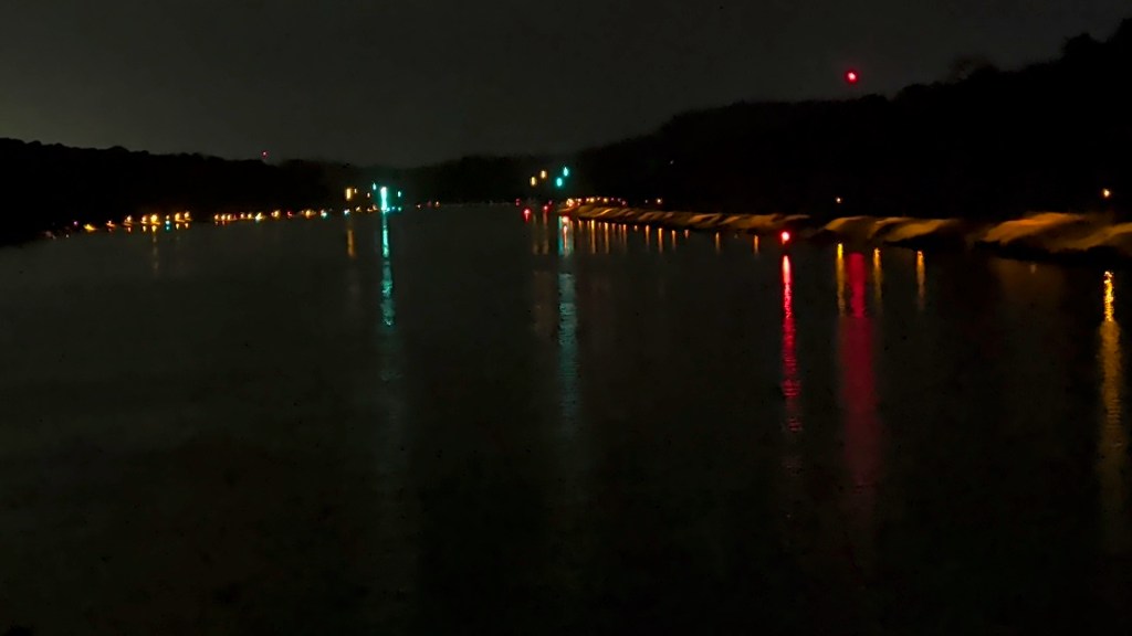 Nighttime view of a river reflecting various colored lights from nearby structures and traffic signals.