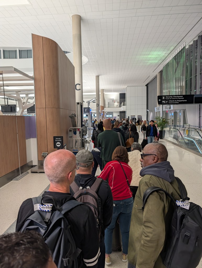 A long line of travelers waiting in an airport terminal near a security checkpoint.