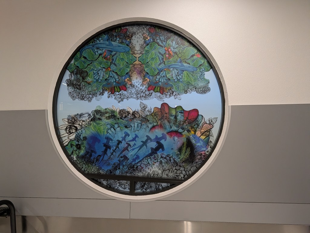 A circular window featuring vibrant artwork of marine life, including fish and underwater plants, framed by intricate designs and patterns.