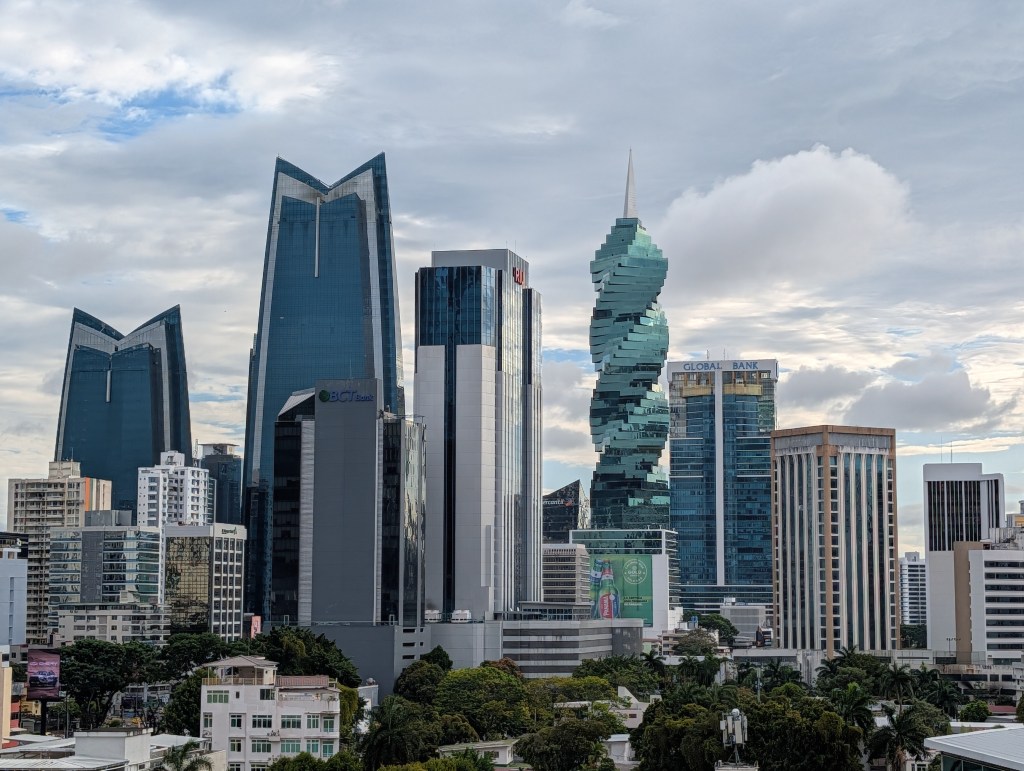 City skyline featuring modern skyscrapers and distinctive architecture, including a twisted building and triangular rooftops under a cloudy sky.