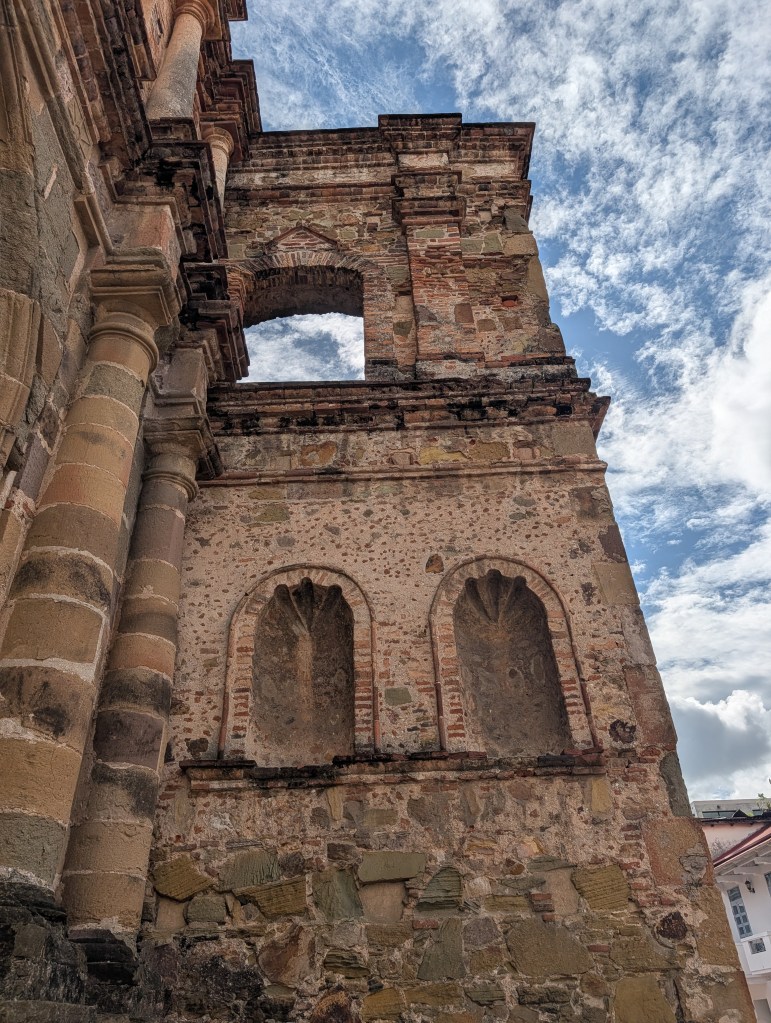 Vertical view of a historic stone wall with decorative architectural features and cloudy sky in the background.