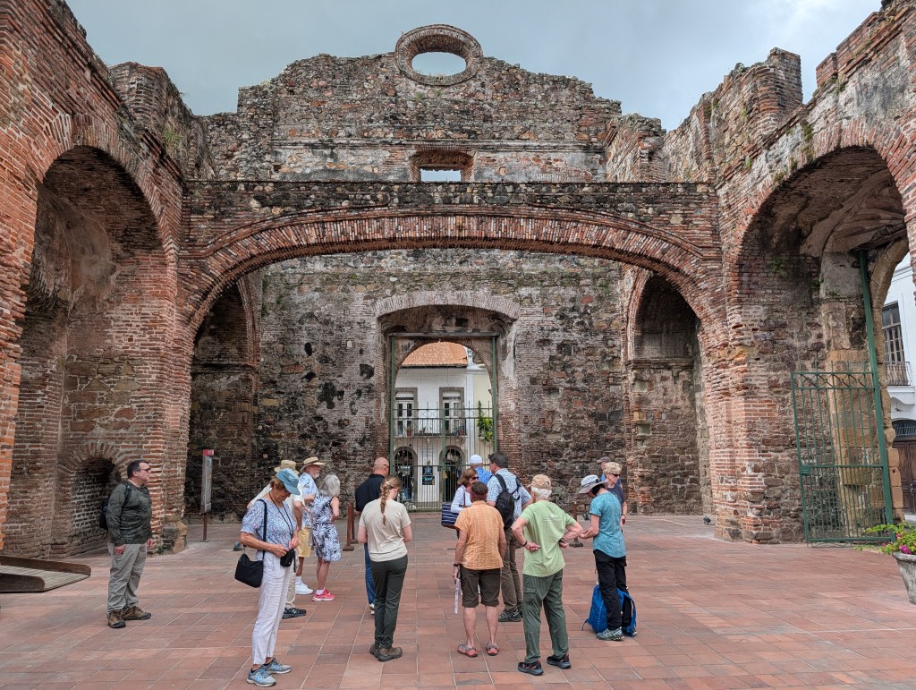 A group of tourists gathered inside the ruins of a historic structure with brick arches and stone walls.