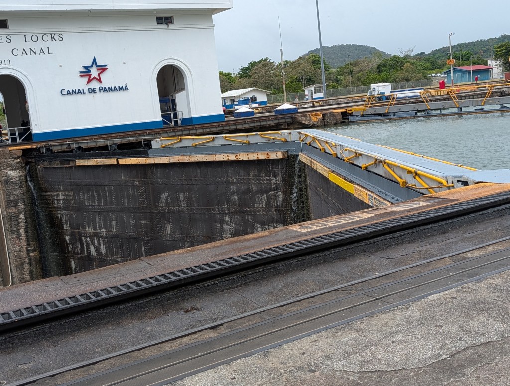 View of the Culebra Cut at the Panama Canal, showcasing the Miraflores Locks with a sign indicating 'Canal de Panamá'. Water levels are visible in the lock chamber, with surrounding infrastructure.
