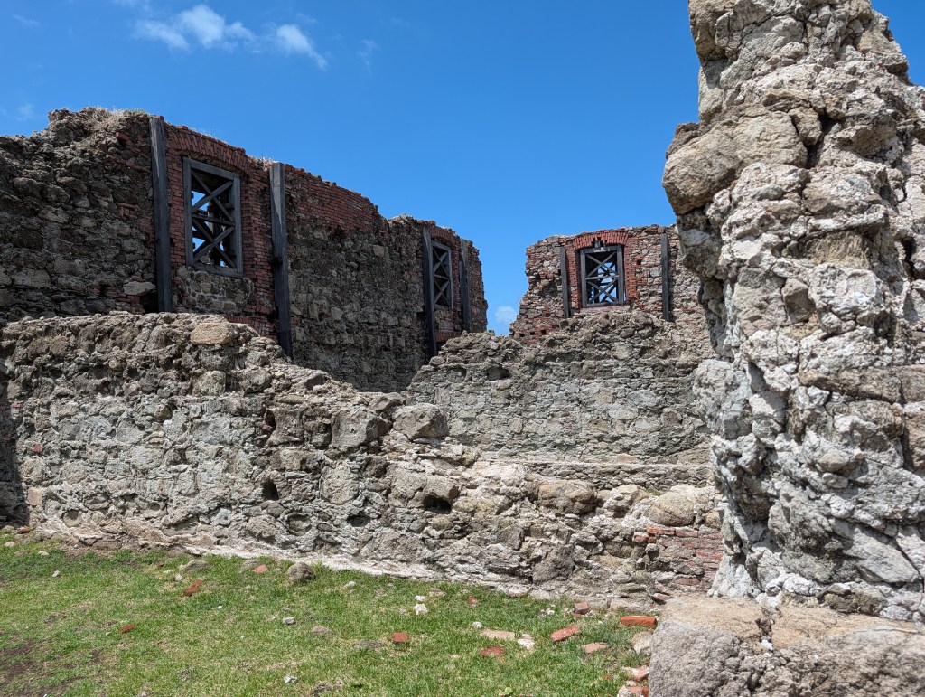 Ruins of an old stone structure with exposed brick walls and wooden beams under a clear blue sky.