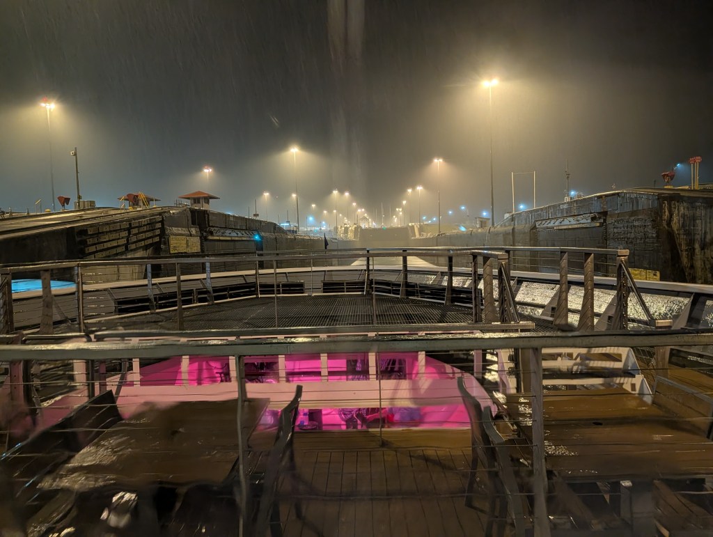 View from a boat at night in a lock chamber, illuminated by artificial lights amid heavy rain.