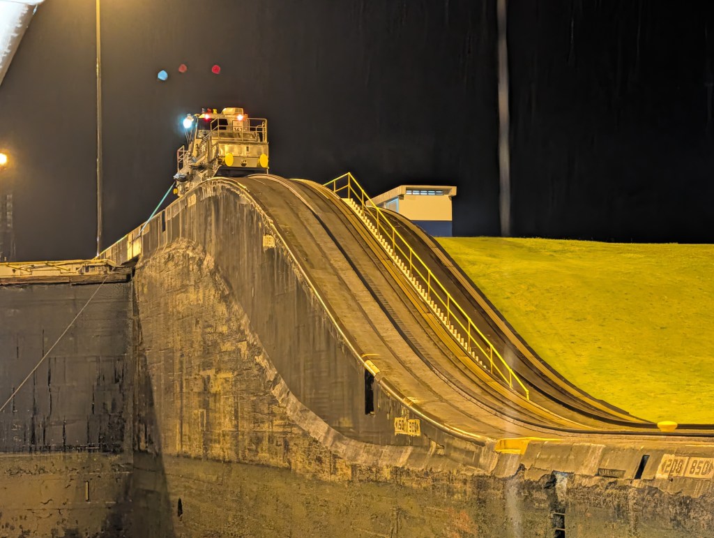A view of a lock chamber at night, featuring a sloped concrete surface leading up to a maintenance vehicle and illuminated by bright lights.