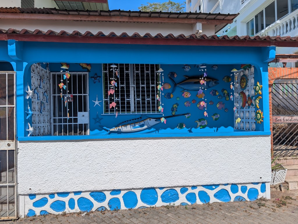 Colorful wall mural of fish and marine life on a blue house exterior, featuring decorative elements like seashells and stars.