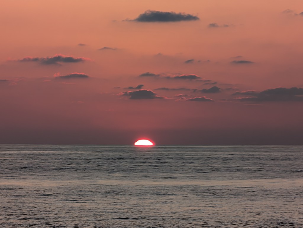 Sunset over the ocean with vibrant colors in the sky and soft clouds.
