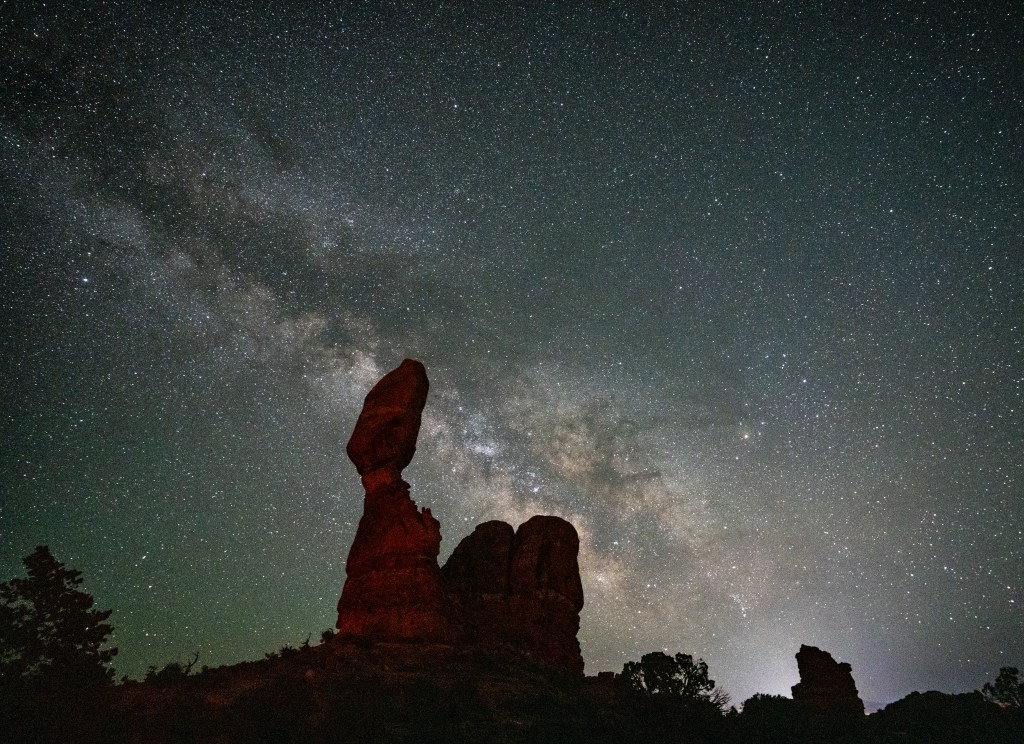 Silhouette of large rock formations under a starry night sky with the Milky Way visible in the background.