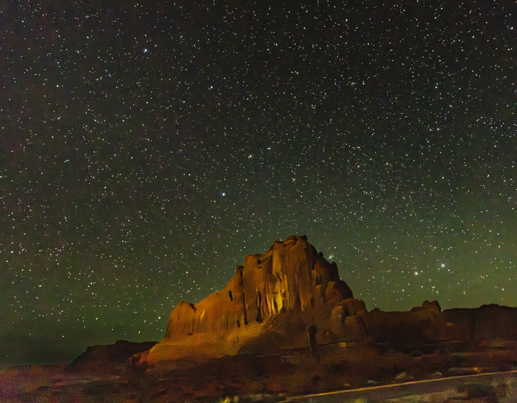 A starry night sky illuminates a rugged rock formation in the foreground, creating a dramatic contrast against the countless stars above.