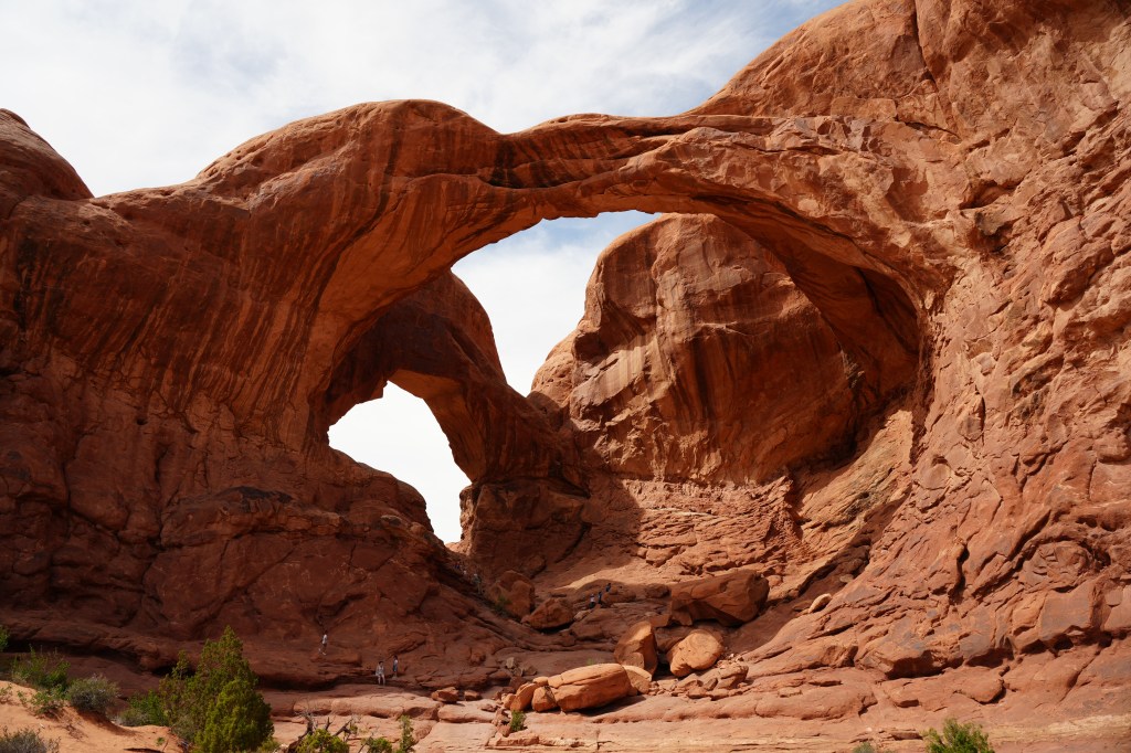 A view of two large sandstone arches in a desert landscape with a clear blue sky.
