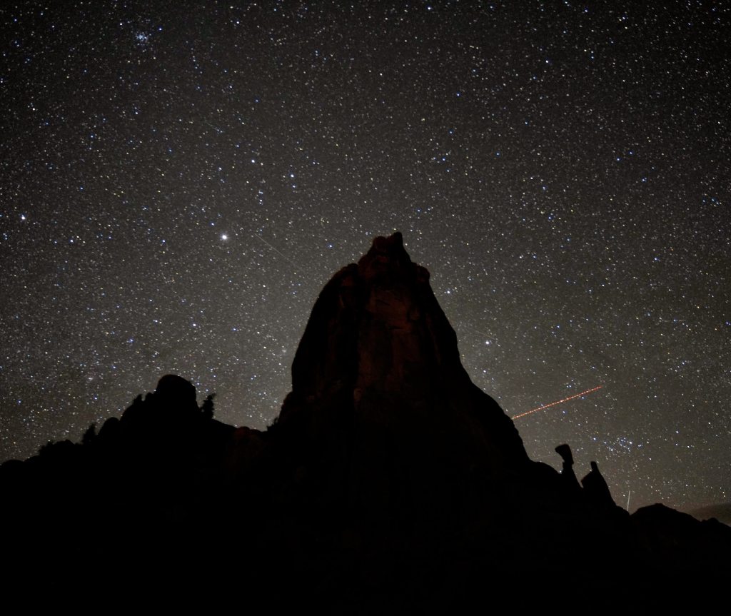 Silhouette of a large rock formation against a starry night sky filled with twinkling stars and distant galaxies.