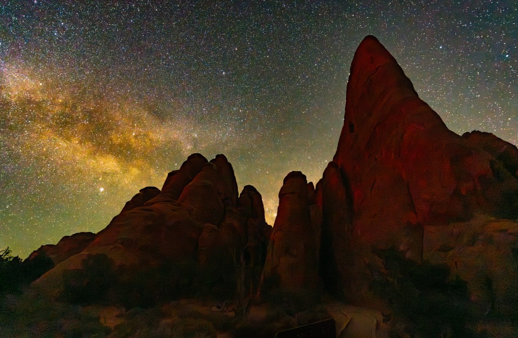 Silhouetted rock formations under a starry night sky with the Milky Way visible.