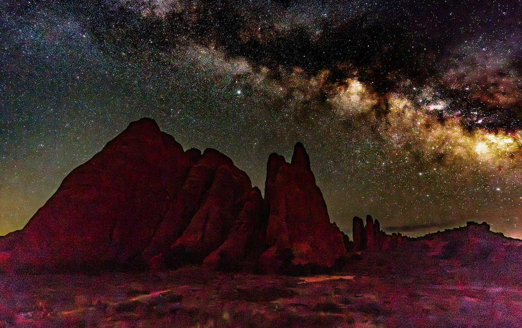 Night sky filled with stars and the Milky Way above dark rock formations.