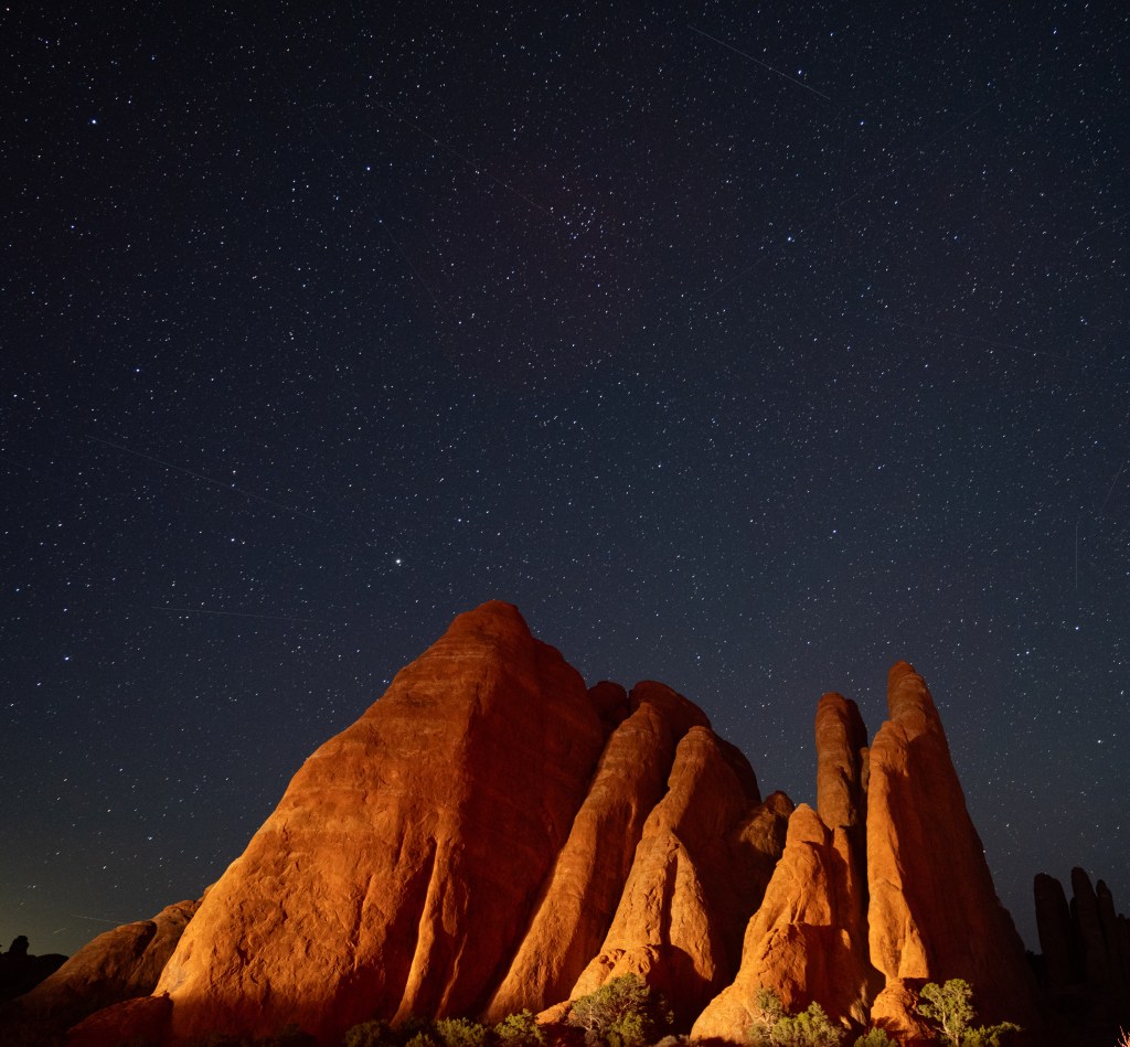 A dramatic night sky filled with stars above illuminated rock formations.