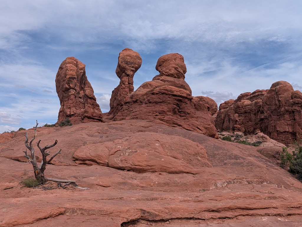View of unique rock formations in a desert landscape with blue skies and scattered clouds.
