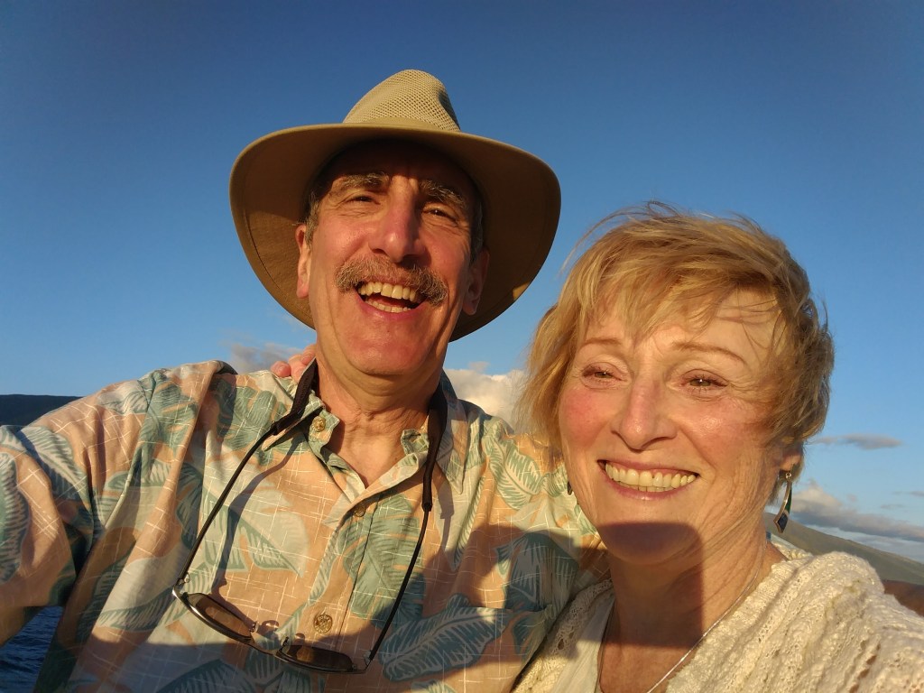 A smiling couple taking a selfie outdoors with a clear blue sky in the background.