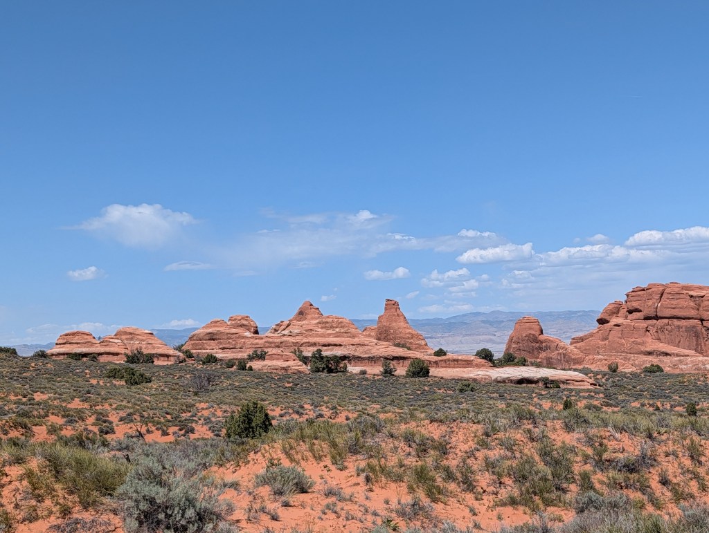 Scenic view of red rock formations under a blue sky with scattered clouds.