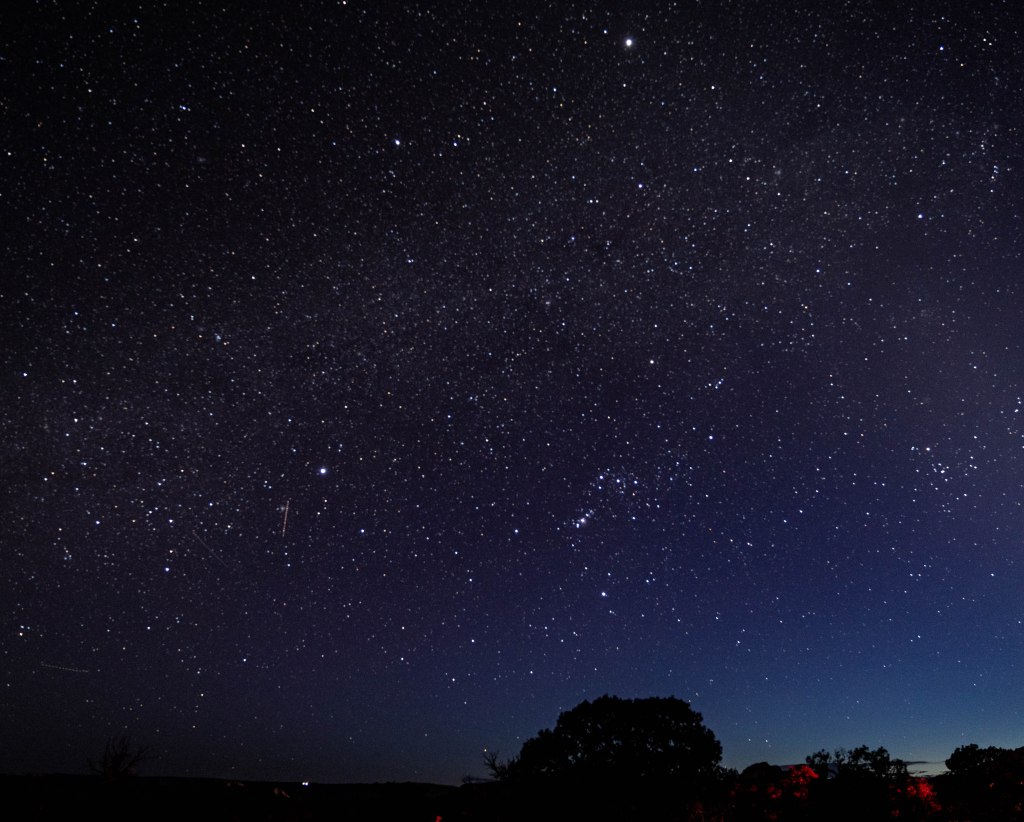 A clear night sky filled with numerous stars and constellations, with a gradient from dark blue to light near the horizon.