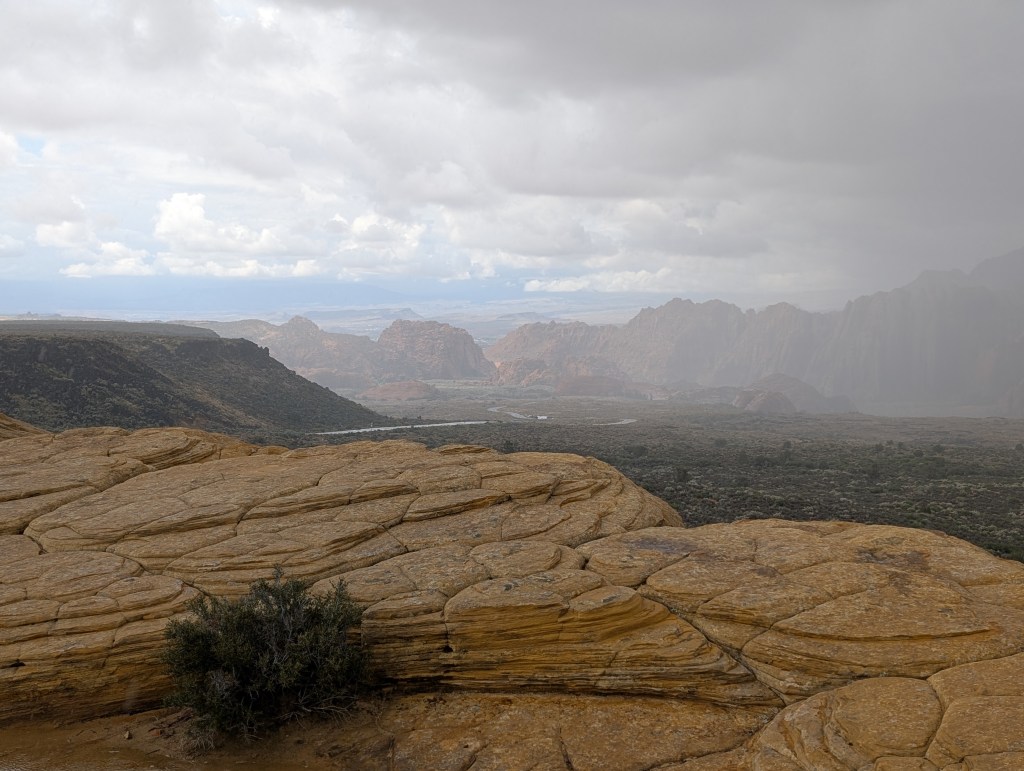 A scenic view of a rocky landscape under cloudy skies, showcasing layered rock formations and distant mountains with a hint of fog.