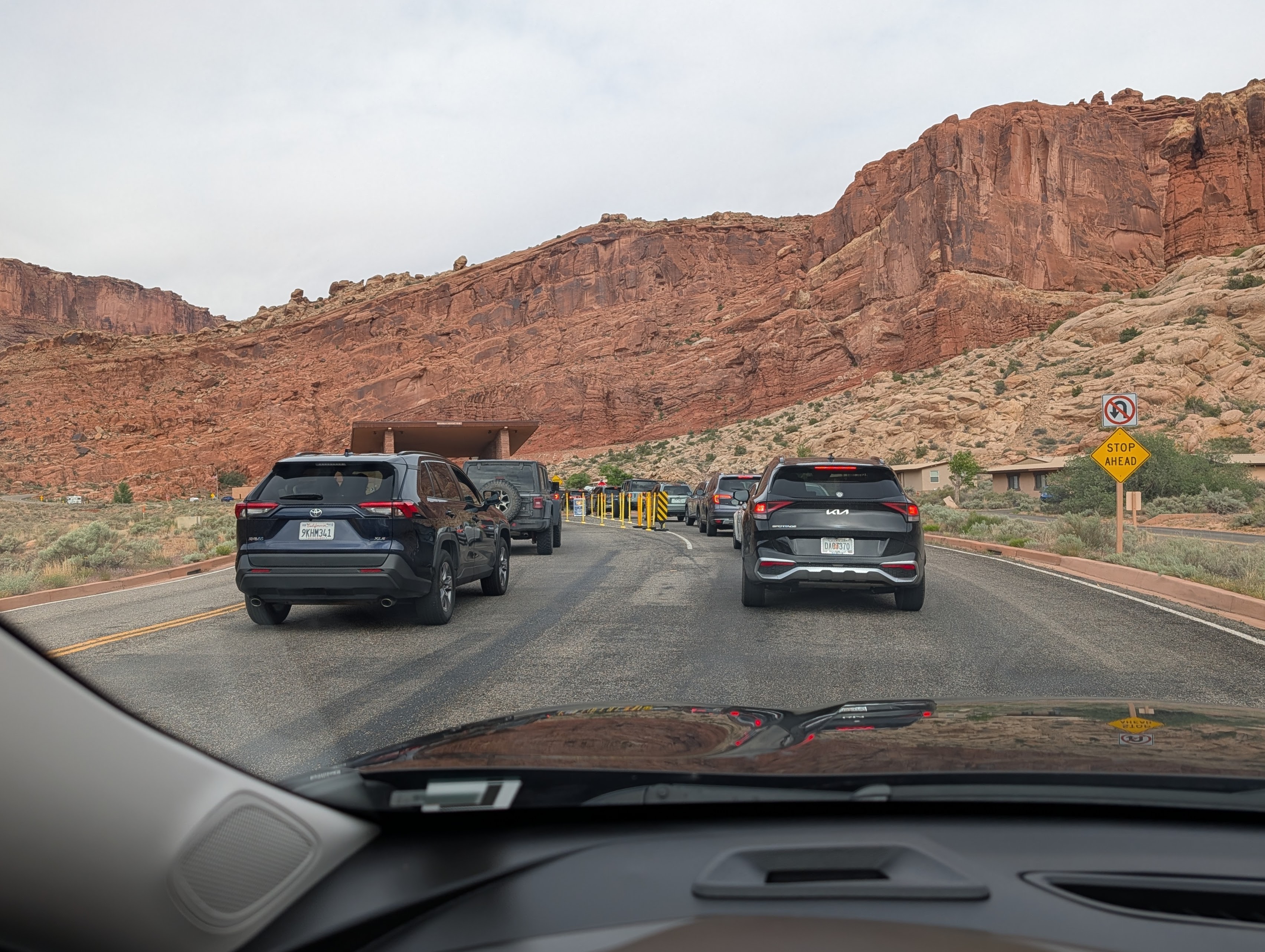Cars waiting in line at a park entrance with red rock formations in the background.