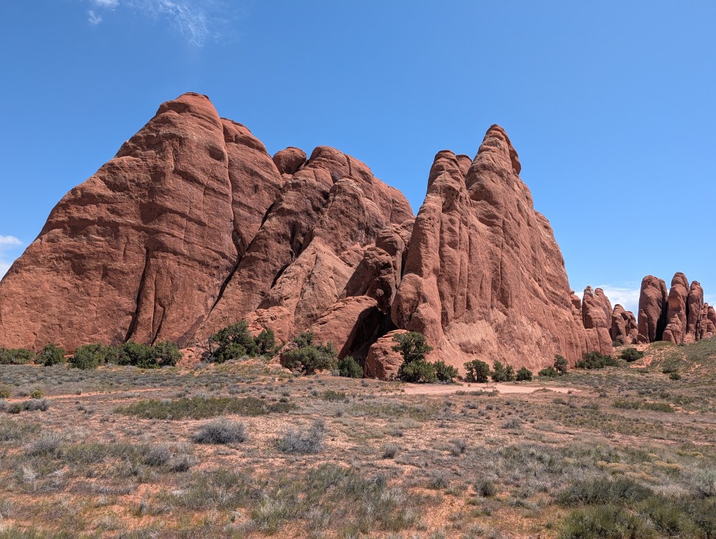 Red rock formations under a clear blue sky with sparse vegetation in the foreground.