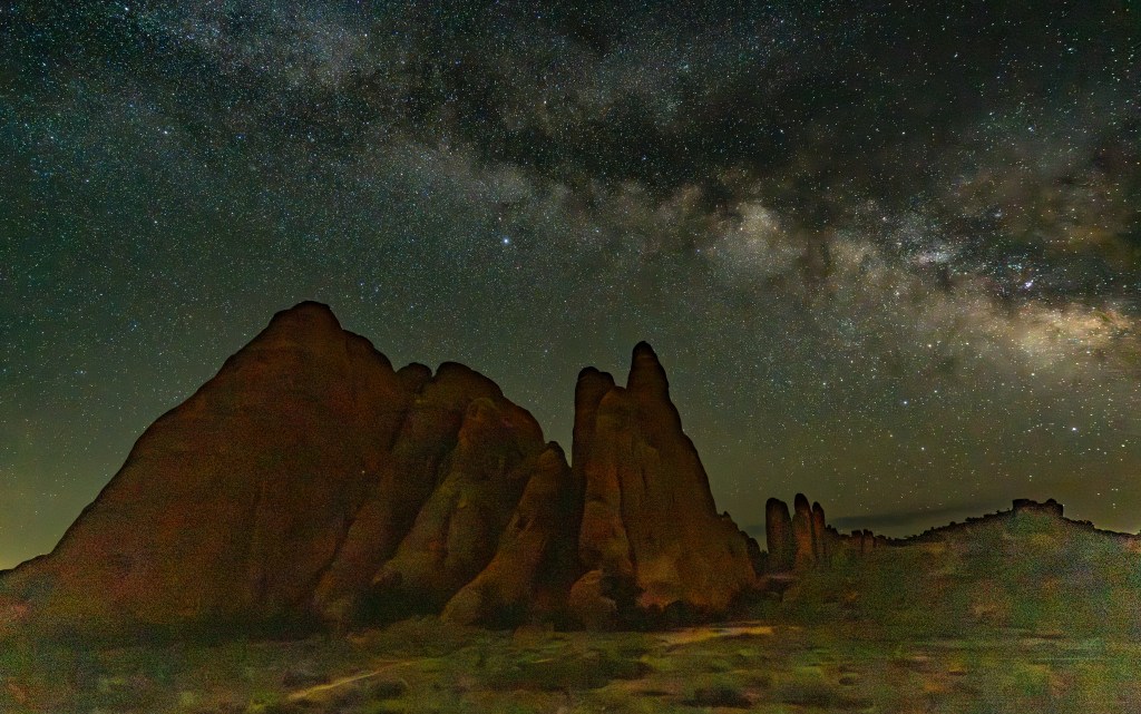 Night sky filled with stars and the Milky Way over towering rock formations.