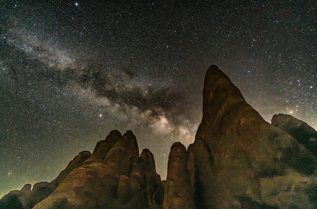 A night sky filled with stars above jagged rock formations, showcasing the Milky Way galaxy.
