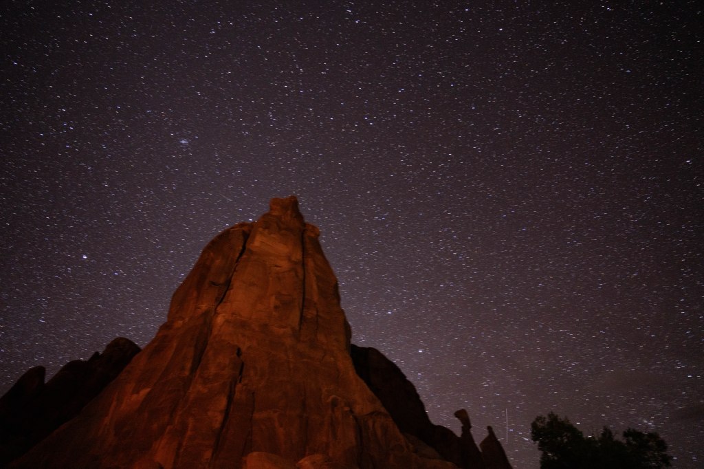A stunning night sky filled with stars above a rocky formation, illuminated by a soft orange glow.