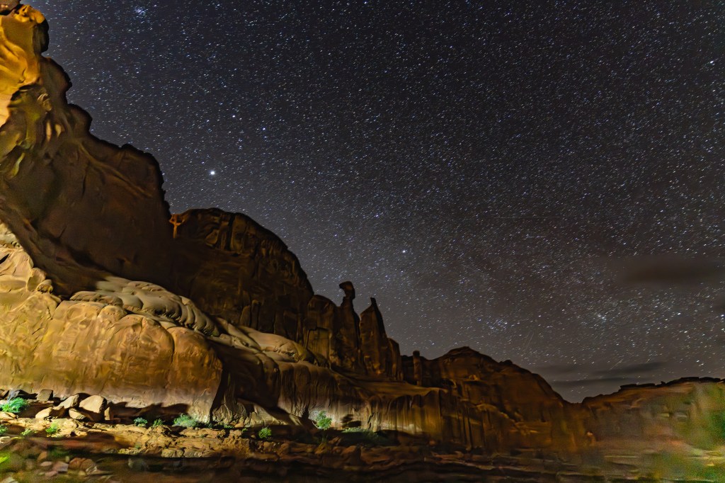 A panoramic view of a rocky landscape under a starry night sky, showcasing a dramatic rock formation illuminated by soft lighting.