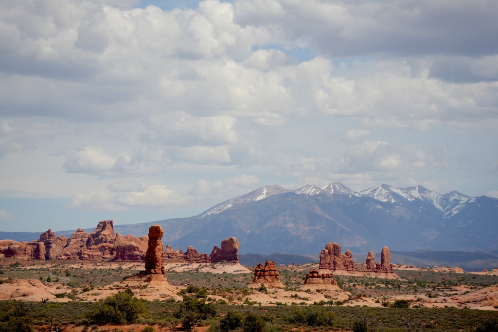 A panoramic view of unique rock formations against a backdrop of mountains and a partly cloudy sky.