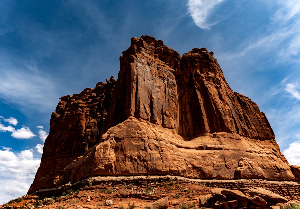 A towering rock formation under a clear blue sky with scattered clouds.