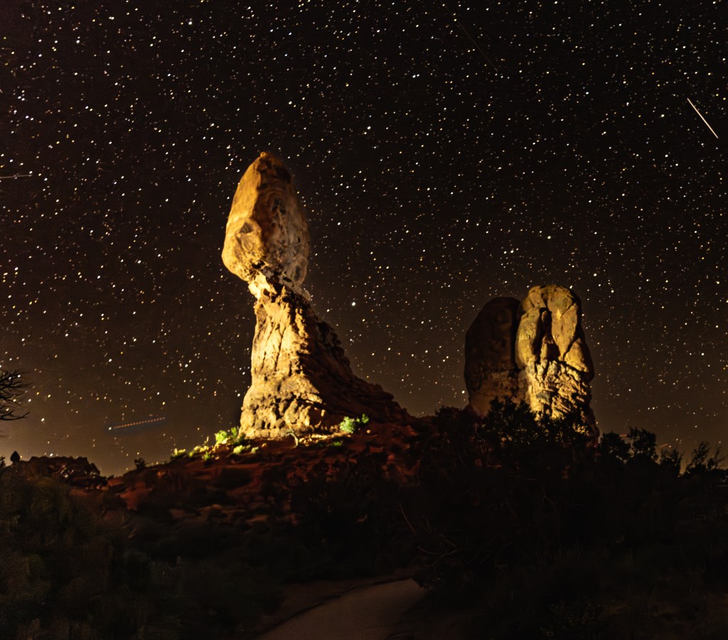 Night landscape featuring towering rock formations illuminated under a starry sky.