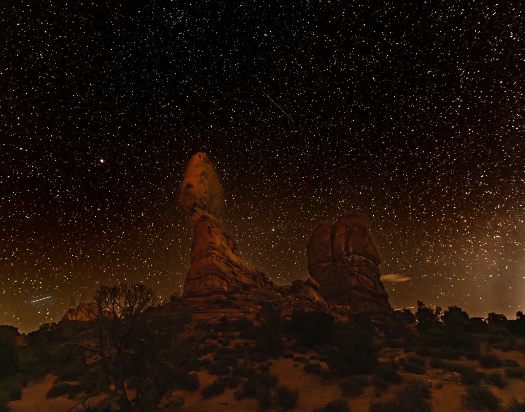 A nighttime landscape featuring two large rock formations under a star-filled sky with numerous stars and faint celestial objects.