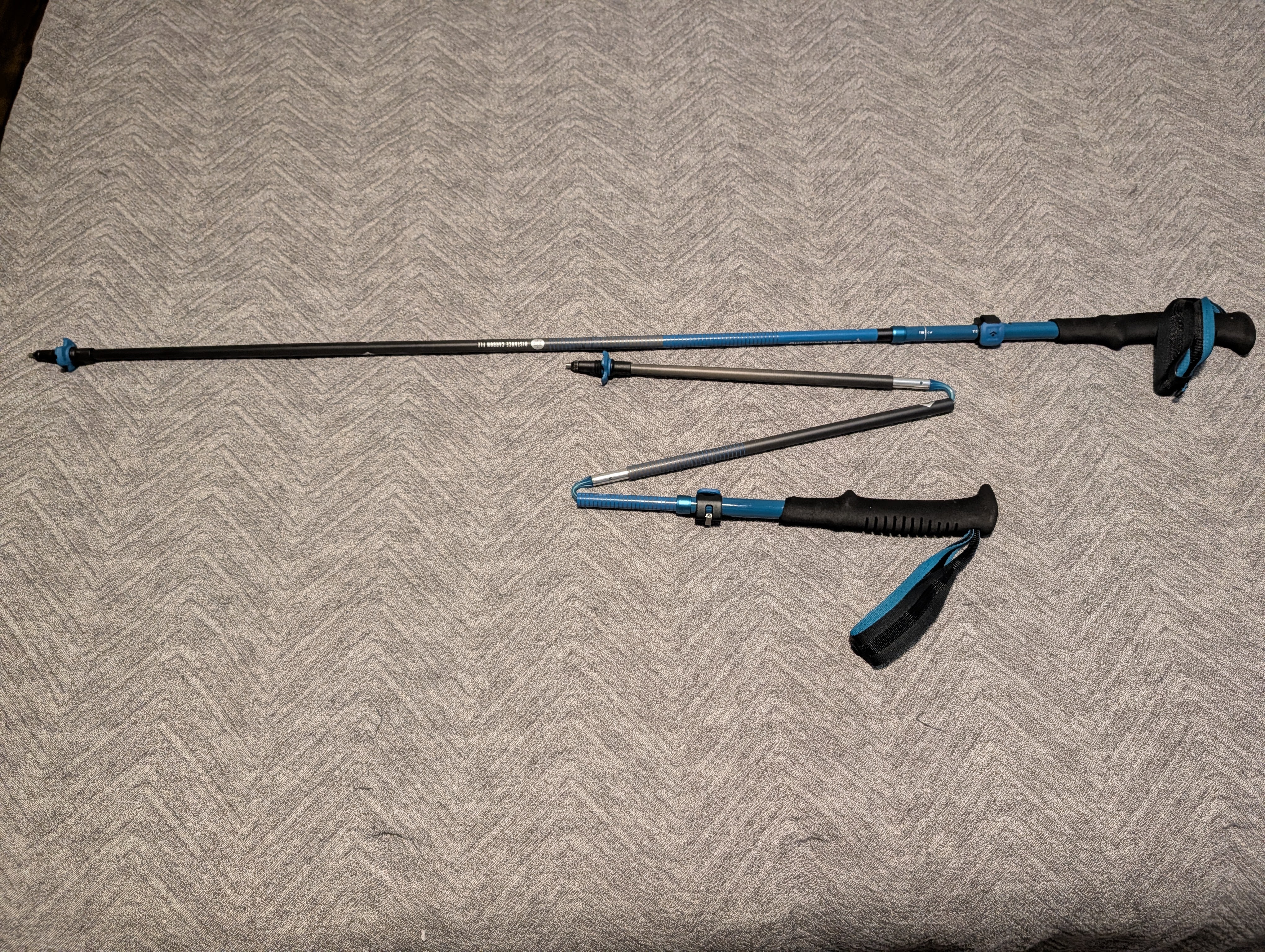 Adjustable trekking poles with blue accents, placed on a textured gray surface.