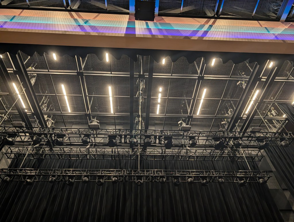 View of a theater ceiling with overhead lighting and rigging, showcasing a grid of lights and equipment above a stage.