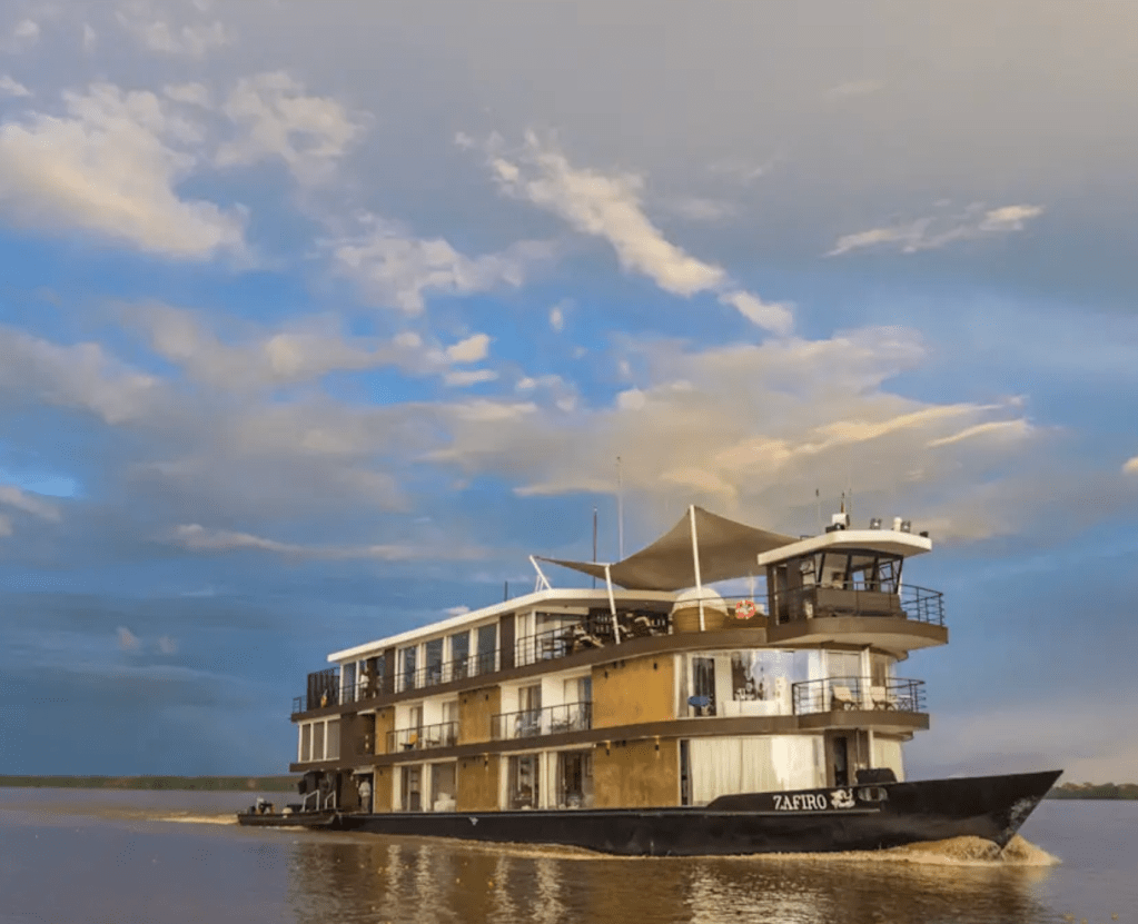 A luxurious riverboat named Zafiro cruising on calm waters under a partly cloudy sky.