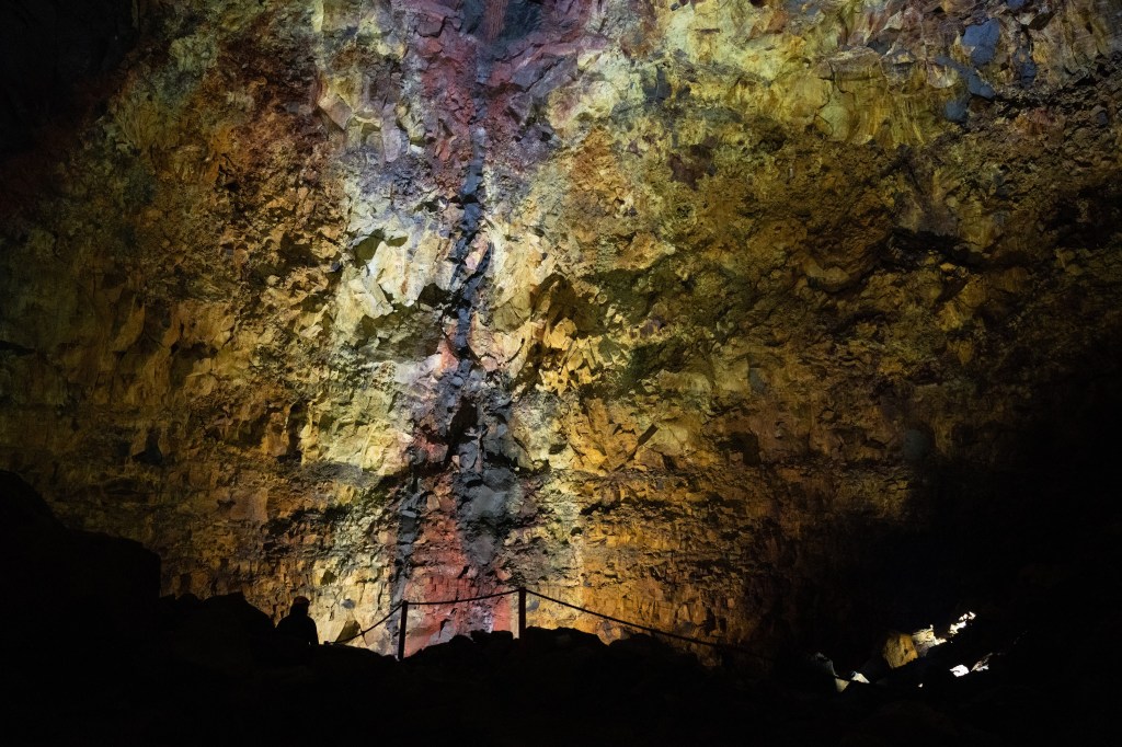 Inside a colorful cave, featuring illuminated rock formations and a silhouetted person observing the scene.