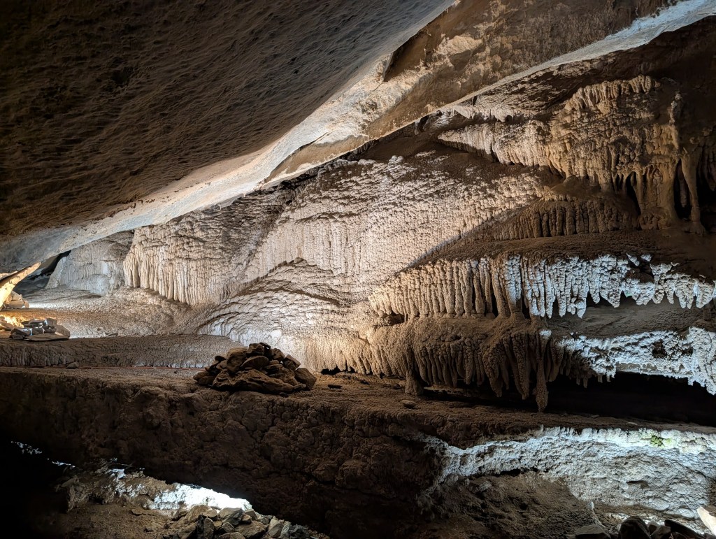 Interior view of a cave showcasing illuminated stalactites and stalagmites with textured rock formations.
