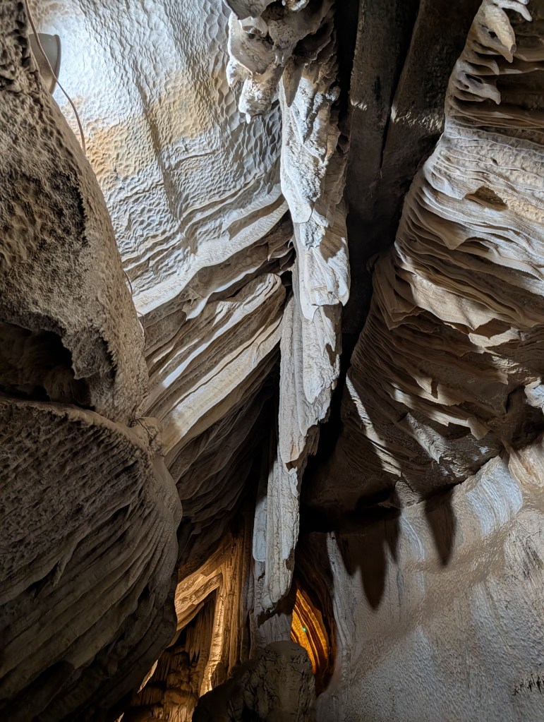 View of a cavernous space with textured rock formations, illuminated from above, showcasing natural patterns and shadows.