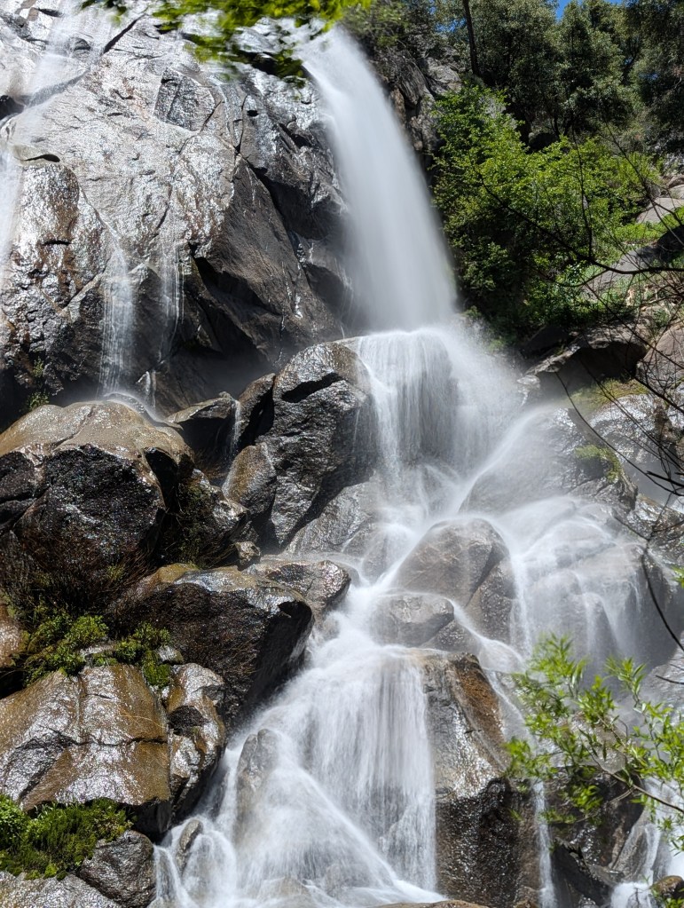 A cascading waterfall flowing down rugged rocks, surrounded by lush green vegetation.