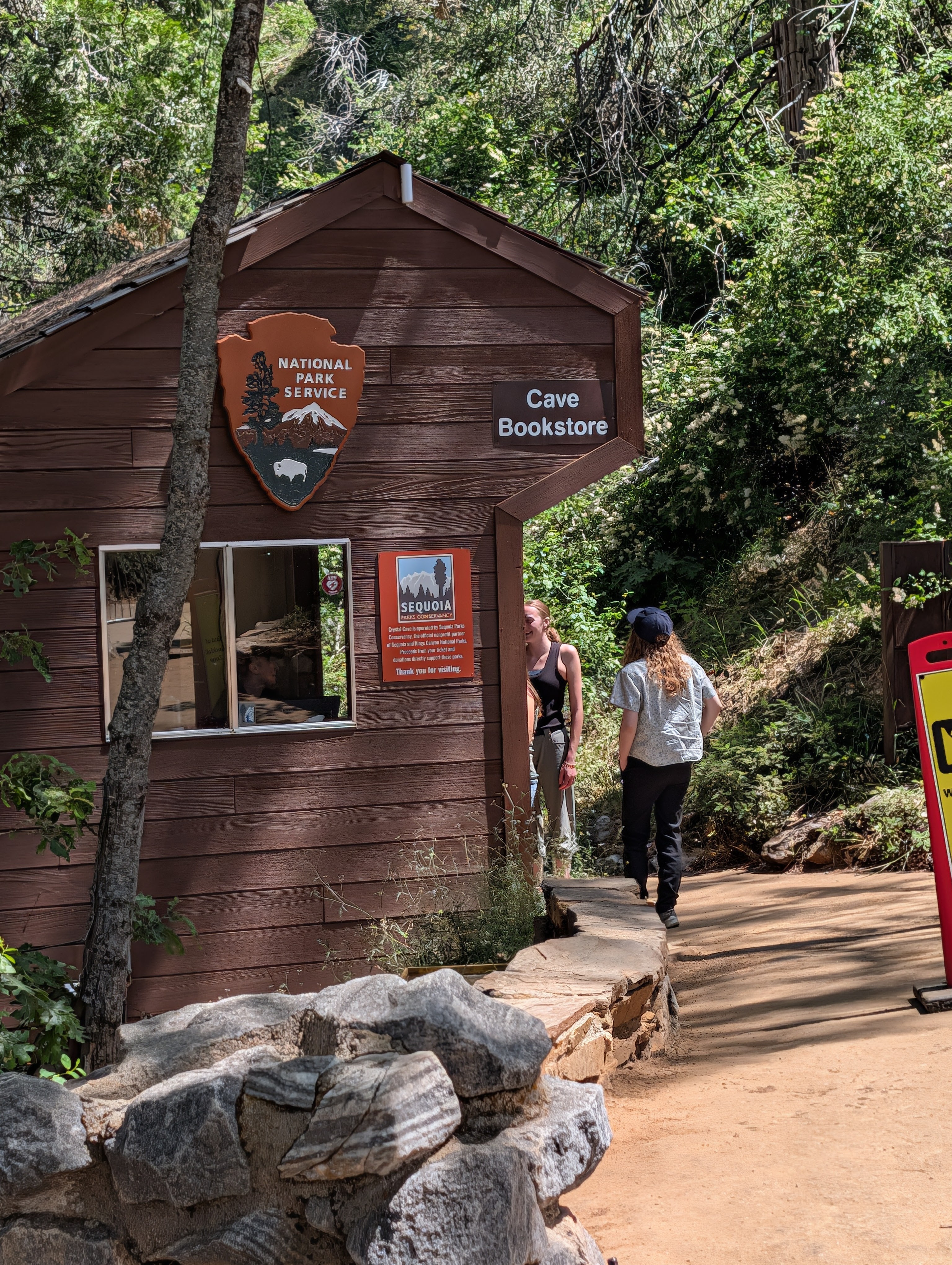 A small wooden building labeled 'Cave Bookstore' with a National Park Service emblem, surrounded by trees and visitors.
