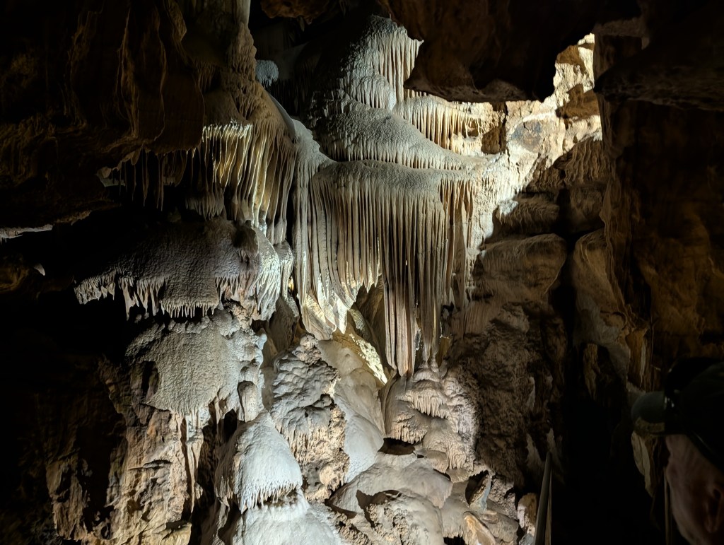 Interior of a cave featuring dramatic stalactites and stalagmites illuminated by soft light.