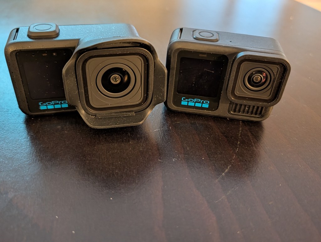 Two GoPro action cameras positioned side by side on a wooden surface.