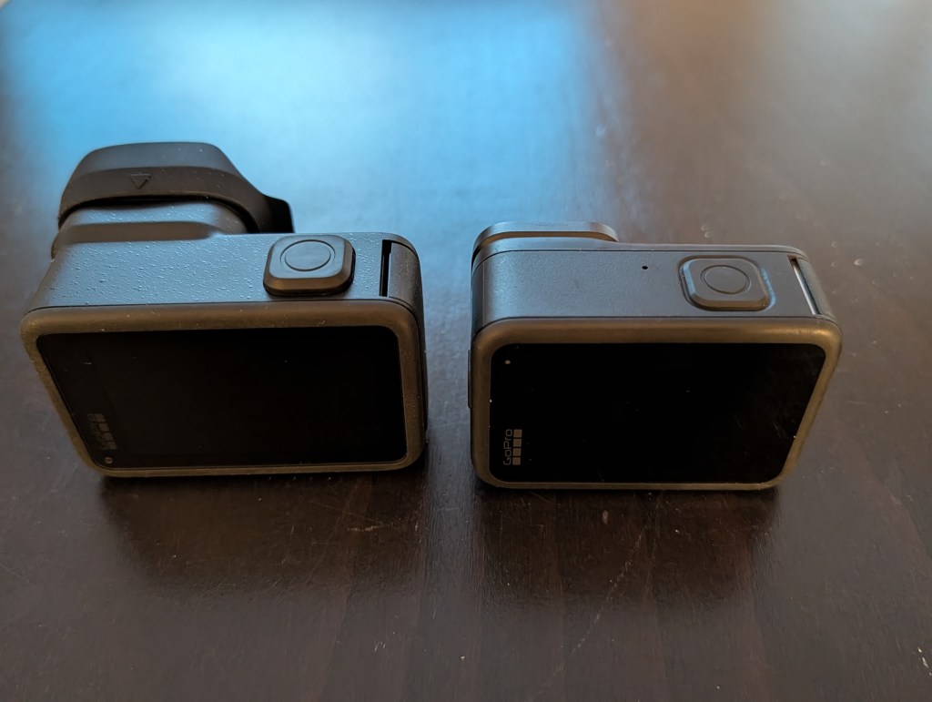 Two GoPro cameras side by side on a wooden surface, showing their sleek black designs and control buttons.