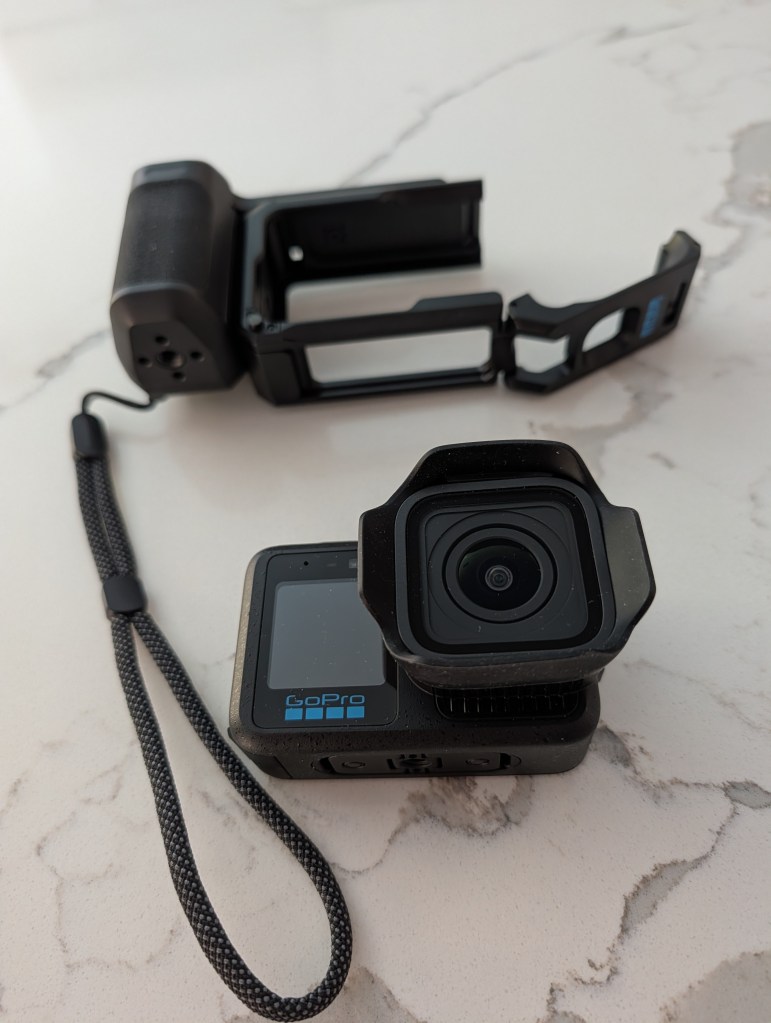 A GoPro camera with a protective case, laid on a marble surface. The camera features a front display and a strap attached for secure handling.