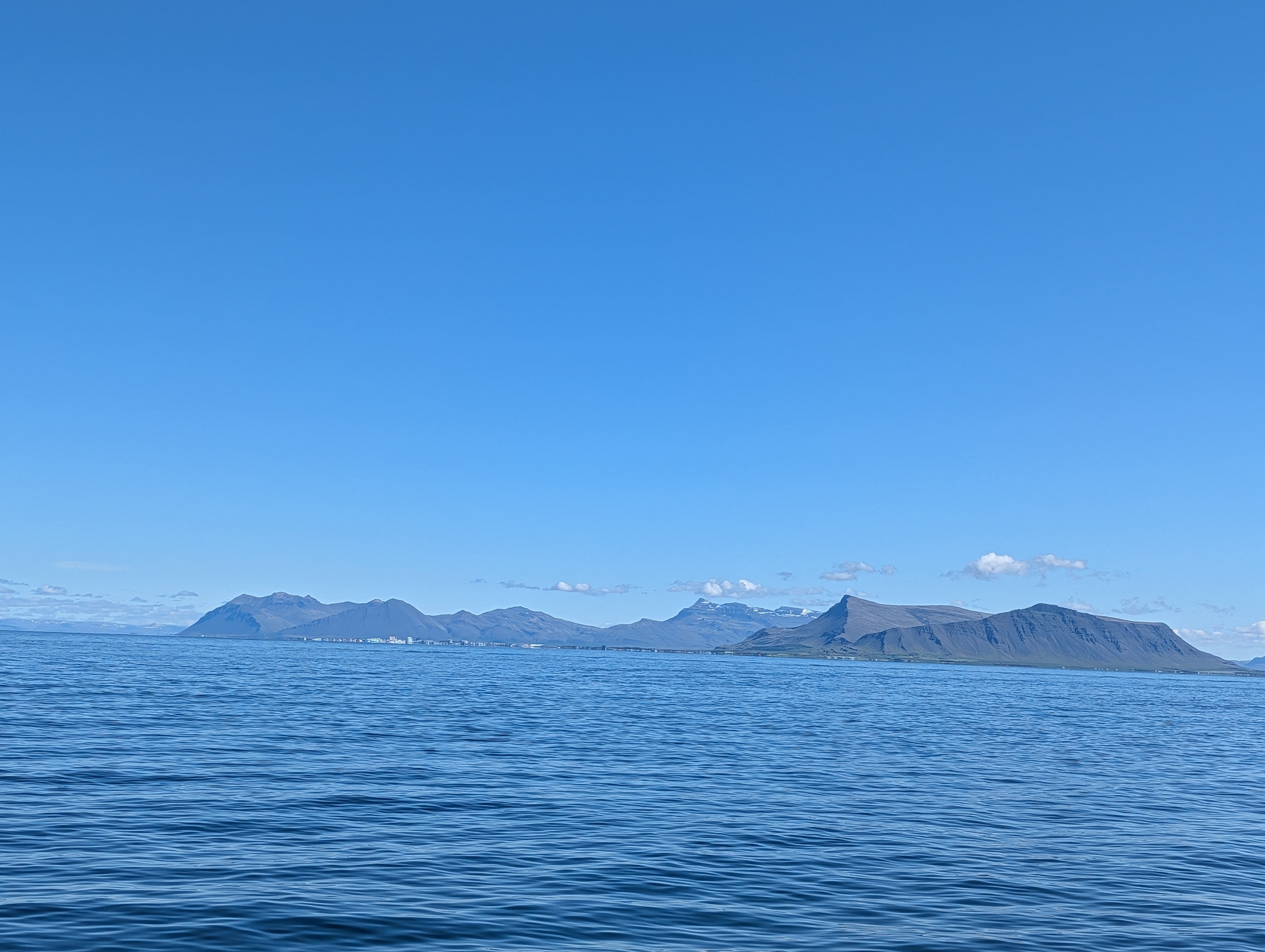 Panoramic view of a calm ocean with distant mountains under a clear blue sky.