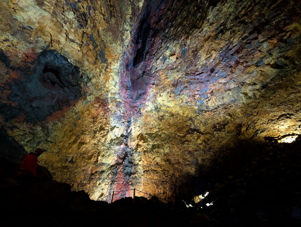 A dramatic view of a cave interior with colorful rock formations illuminated by artificial lights, showcasing a variety of textures and colors in the stone.