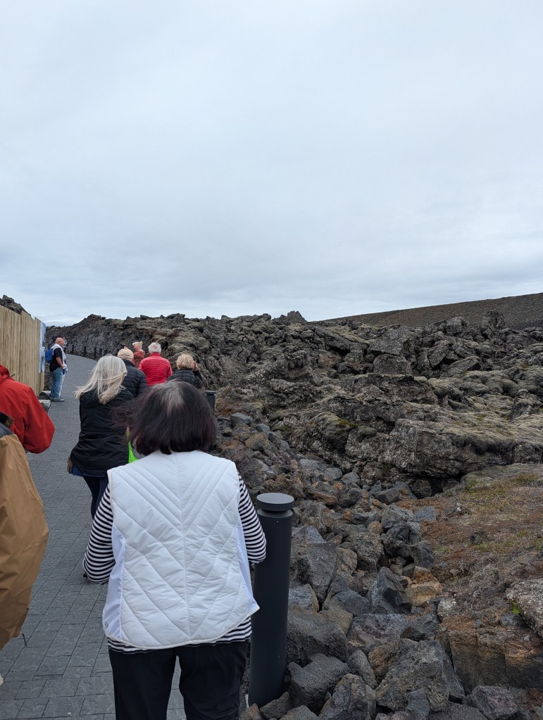 A group of people walking on a pathway surrounded by rocky terrain under a cloudy sky.